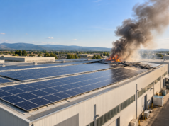 Incendio ai pannelli fotovoltaici della Salpa-Rolli a Roseto: nessun ferito, cause da accertare Illustrazione IA di pannelli fotovoltaici su un capannone industriale con fumo in lontananza.